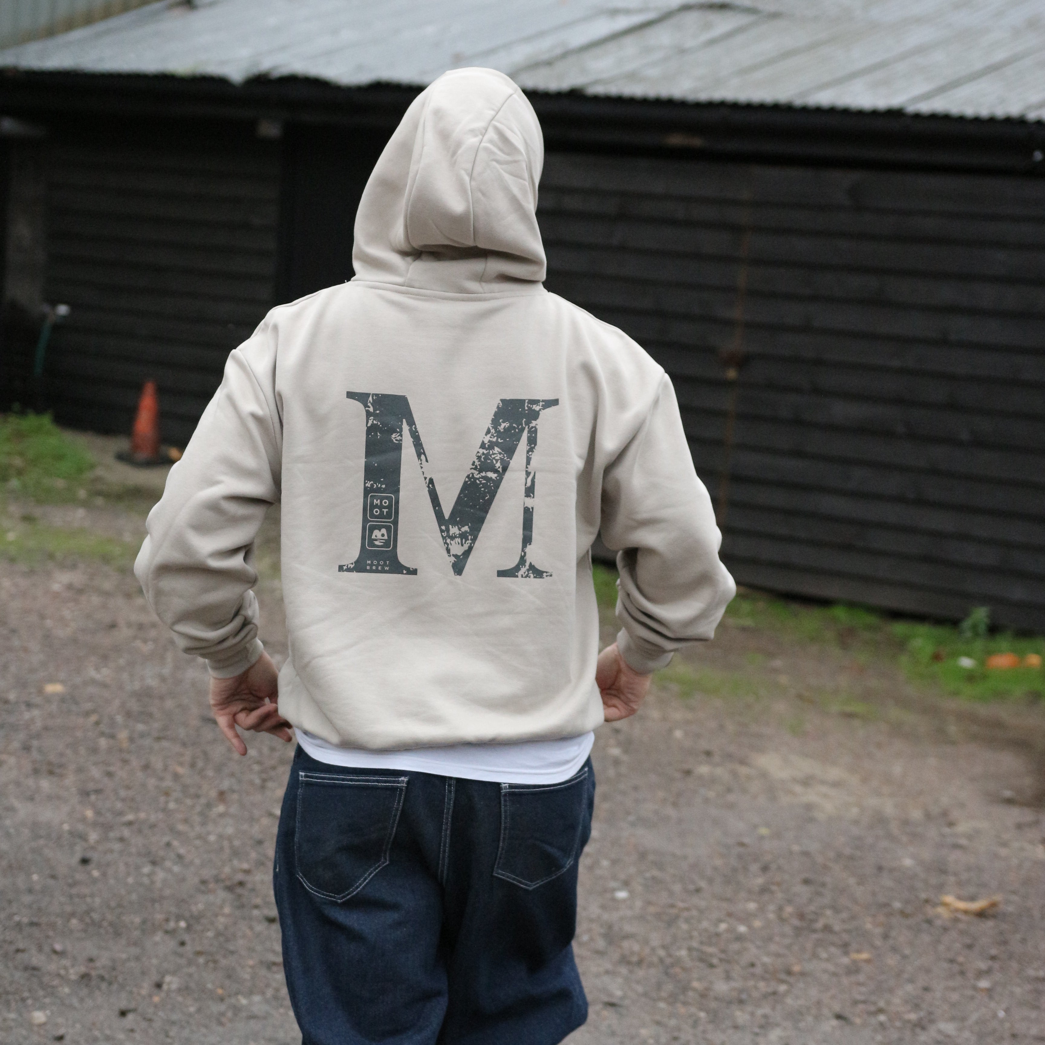Person wearing a beige hoodie with text, standing on a street.