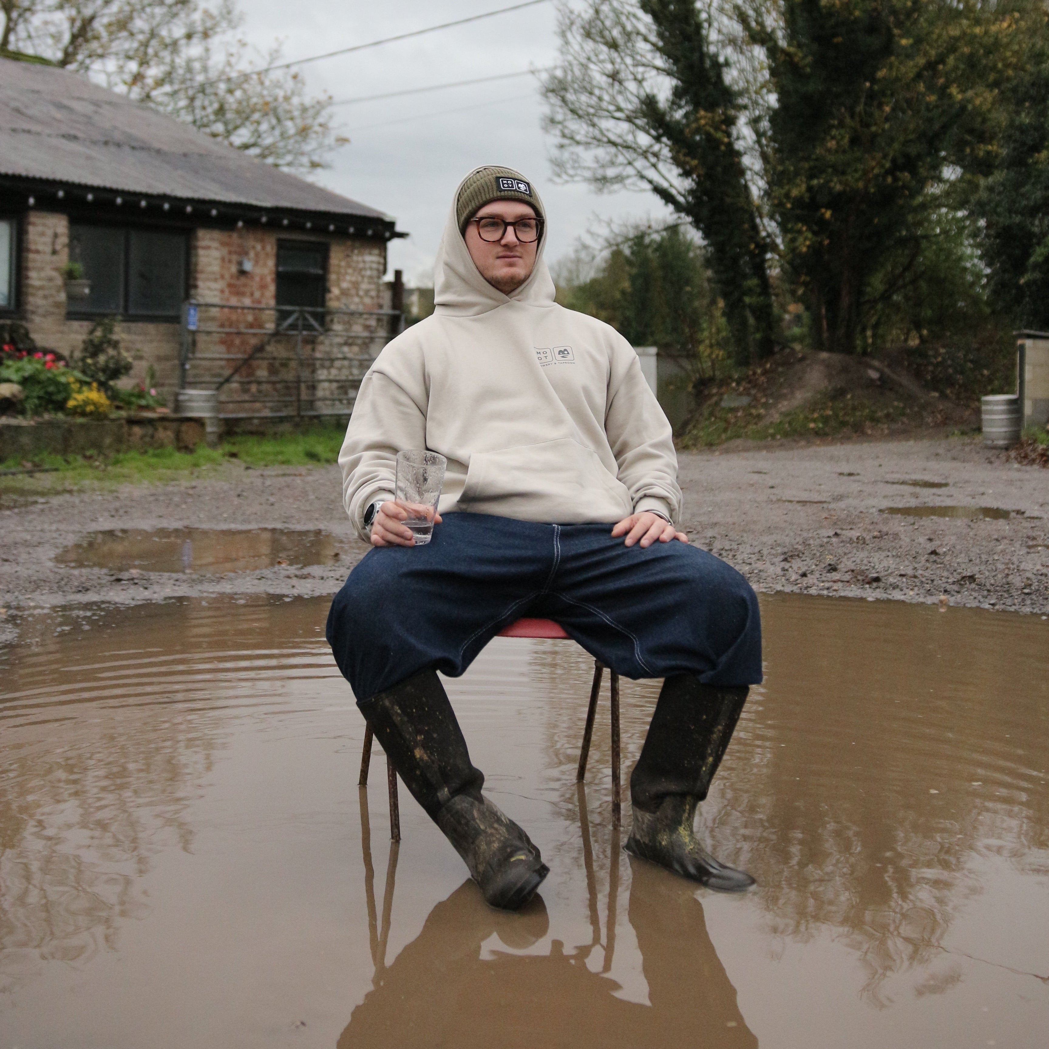 Person standing in a muddy puddle with a house and trees in the background