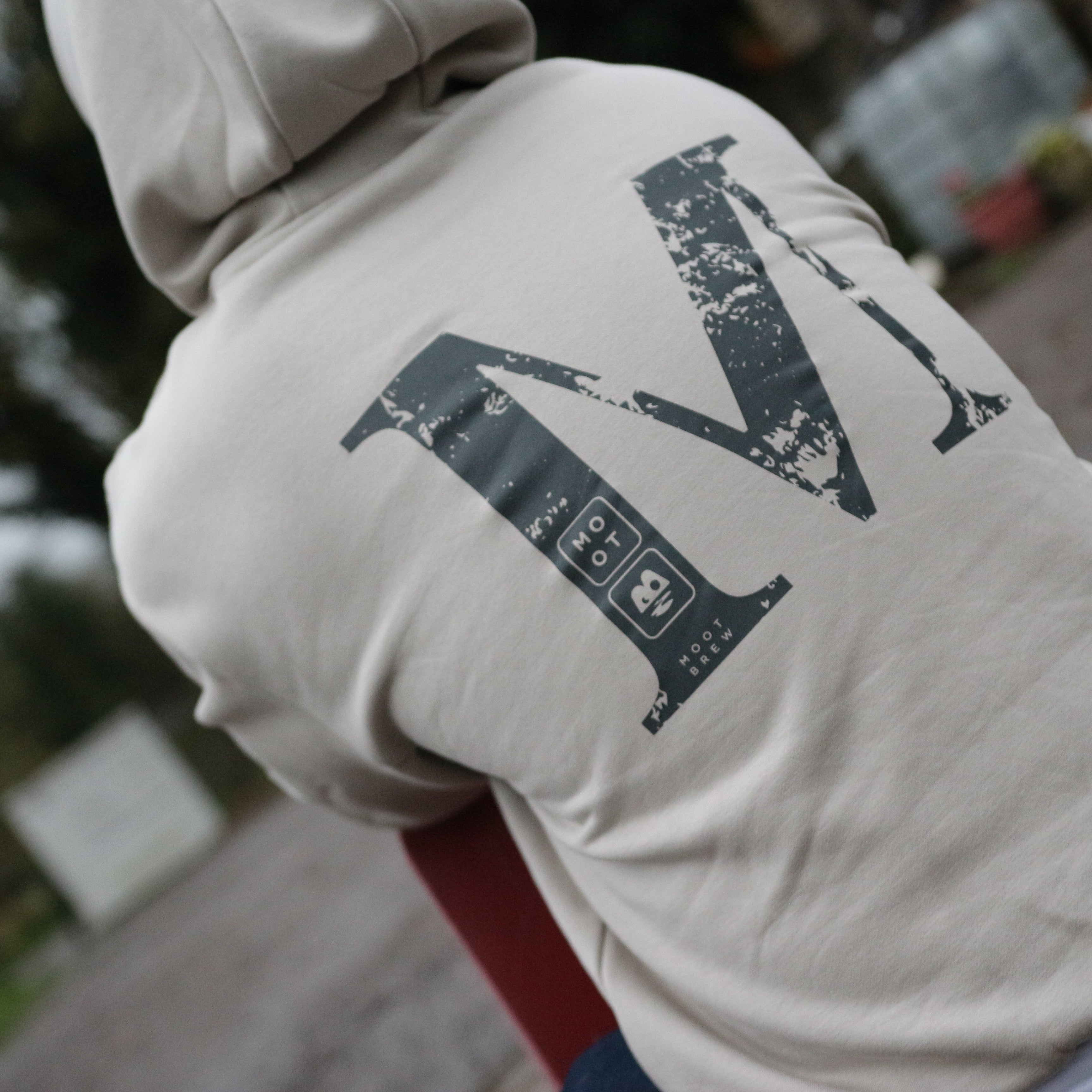 Close-up of a beige hoodie with a black graphic design on the back, outdoors.
