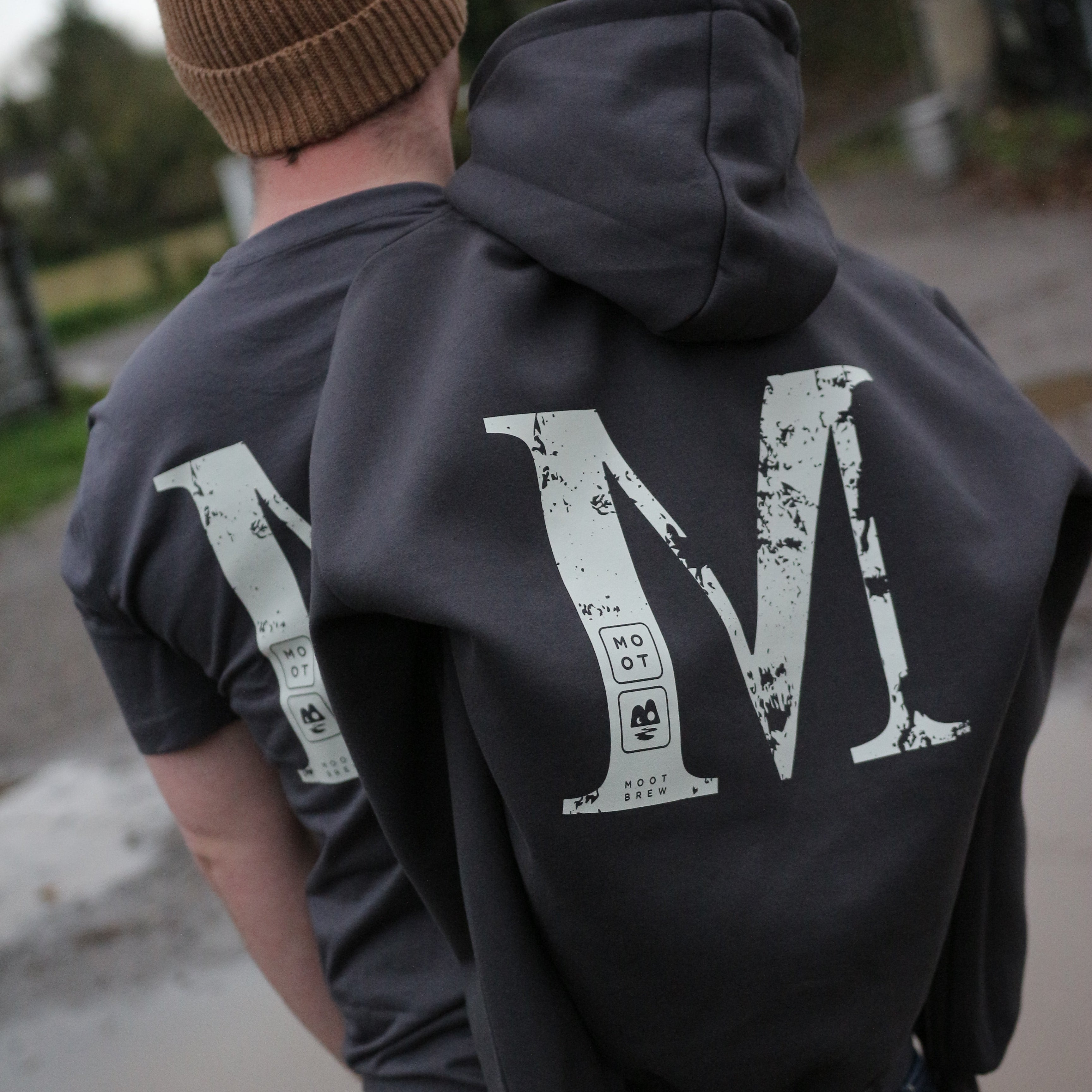 Person wearing a dark jacket with a large white letter 'M' on the back, standing outdoors.